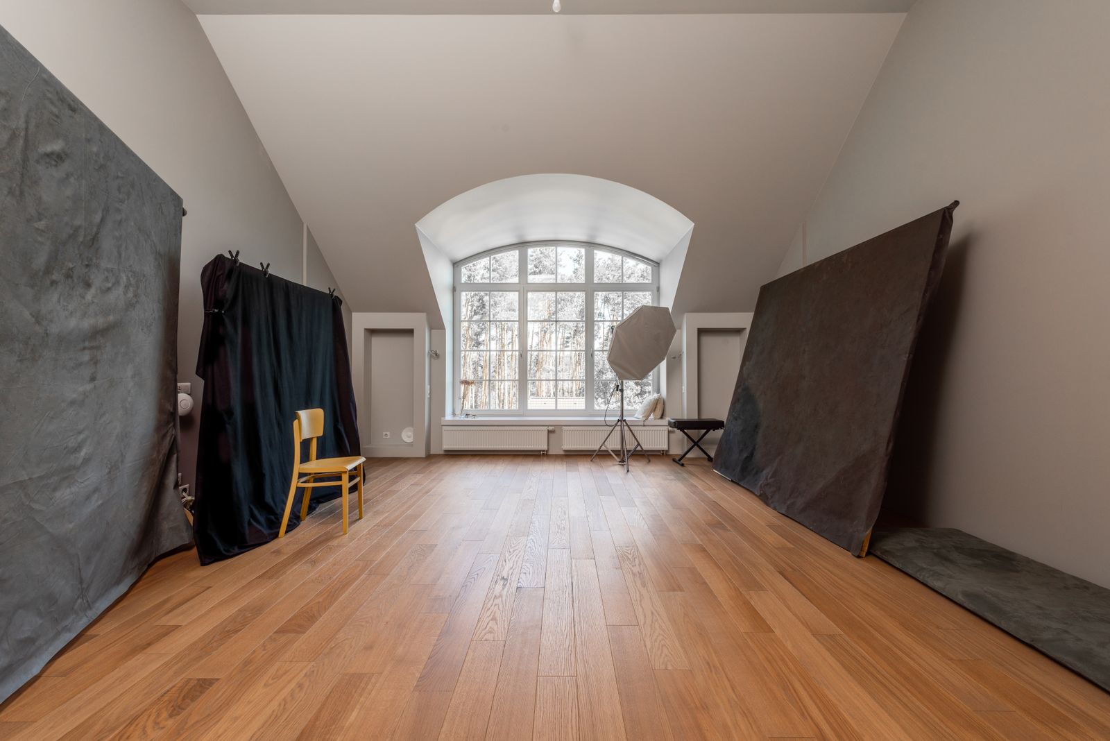 The Solarium — a vaulted, daylight-filled studio room with an arched window and warm wooden floor